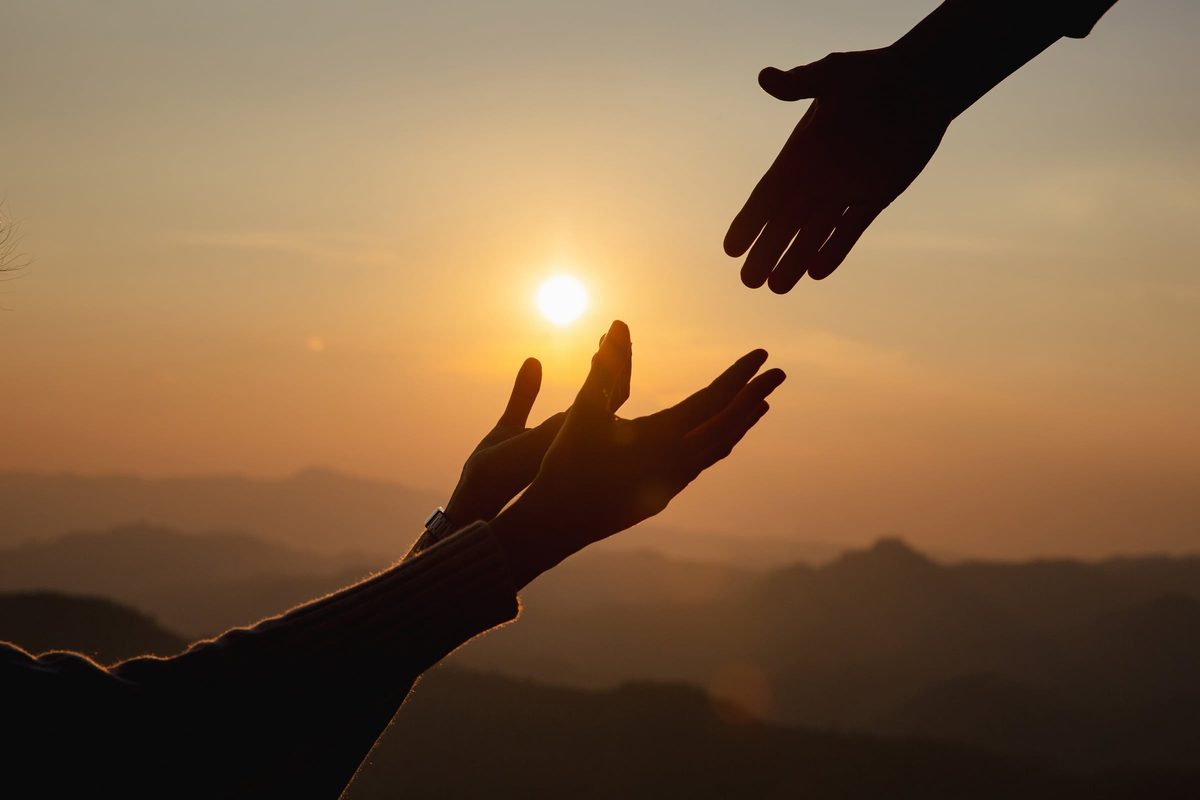 Twee handen reiken naar elkaar bij zonsondergang